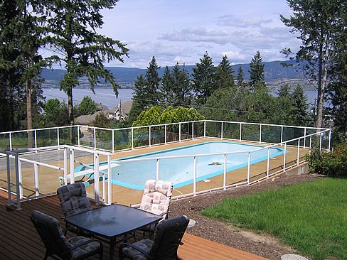 In-ground pool enclosed by a glass rail with a deck and seating