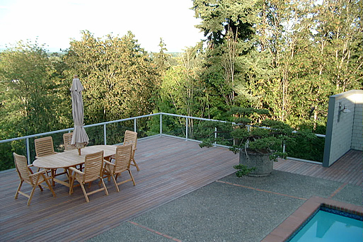 Outdoor dining table on a deck beside a pool with a treeline view
